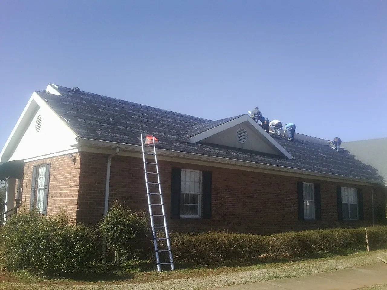 Crew tearing shingles off a brick ranch roof with a ladder set — Emergency Roof Repair work by our crew in Pearson
