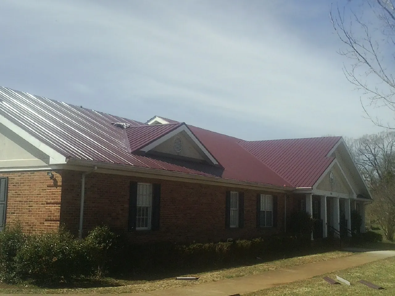 Red metal roof with gabled entries on a long brick building, from a Hail Damage Roof Repair job in Pearson