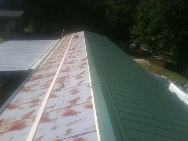 Old rusted panels beside newly installed green metal roofing — Wind Damage Roof Repair by Roofing Brothers in Pearson