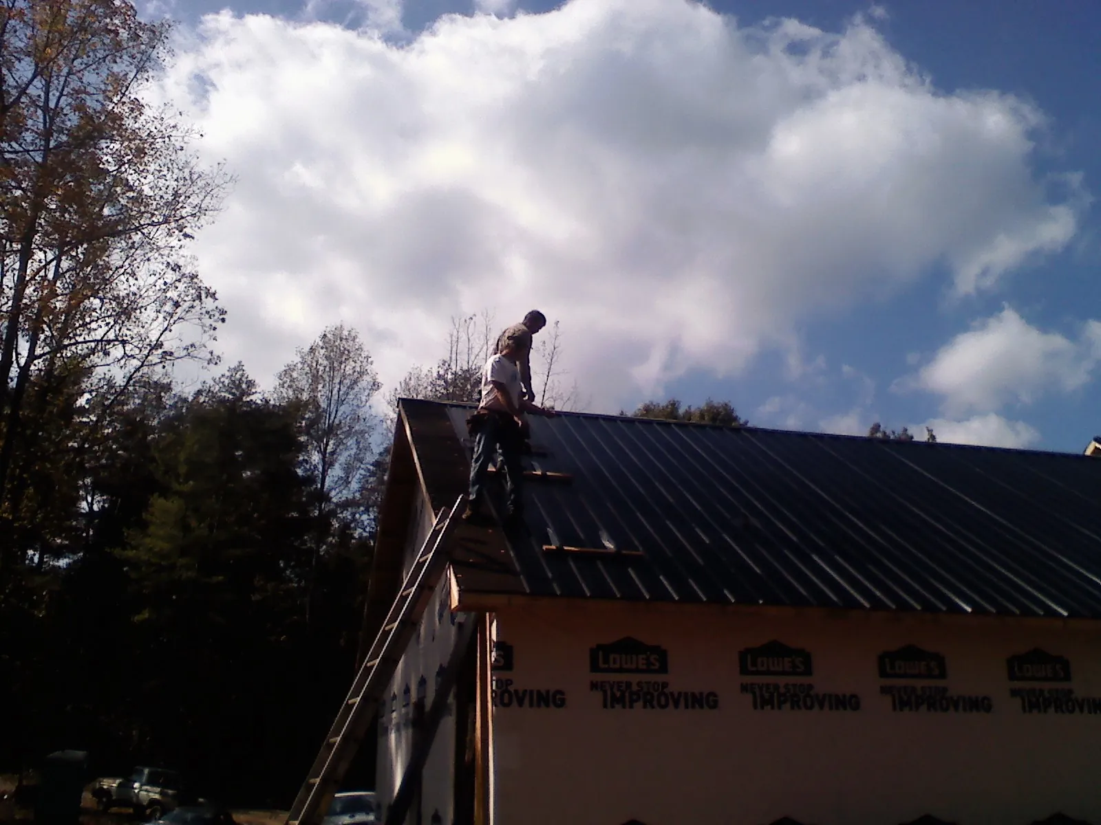 Roofer fastening dark metal panels high against a cloudy sky, from a Roof Inspection job in Pearson