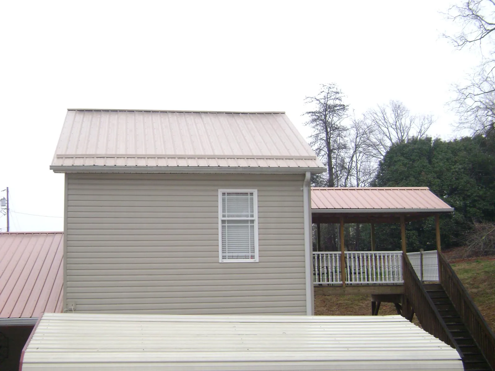 Tan metal roofs on a two story addition and attached porch, from a Roof Replacement job in Pearson